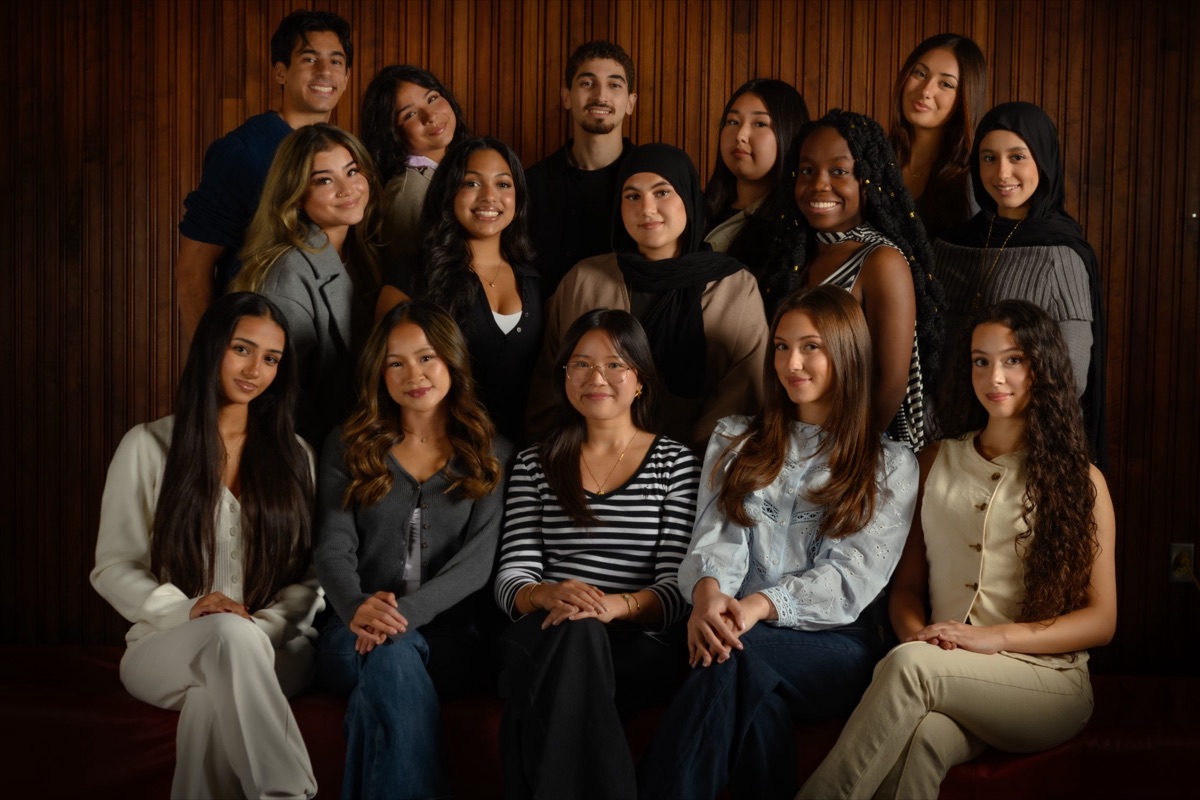 Group portrait of about fifteen young people in three rows, the front row seated, against a dark wood-panelled wall